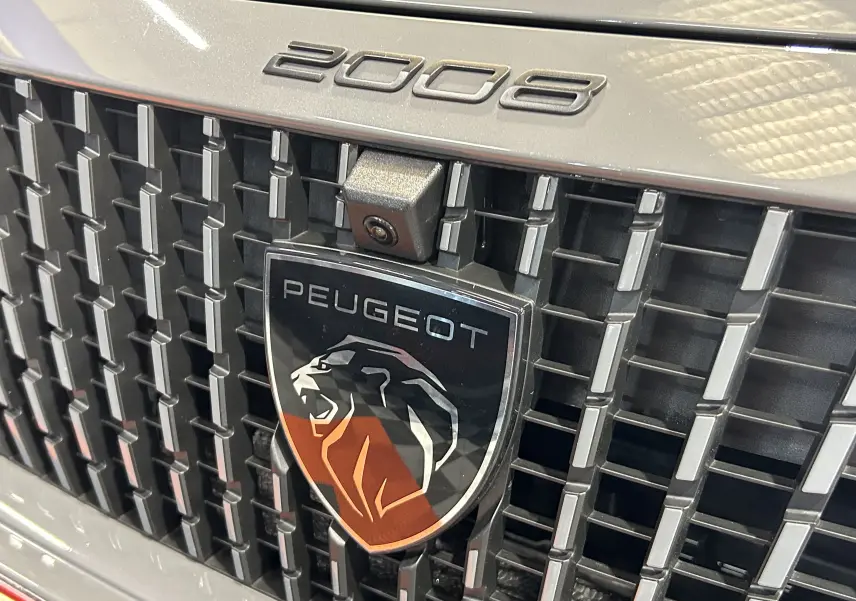 Gros plan sur la calandre gris Selenium du Peugeot 2008 II Ph.2 avec logo lion et caméra frontale intégrée.