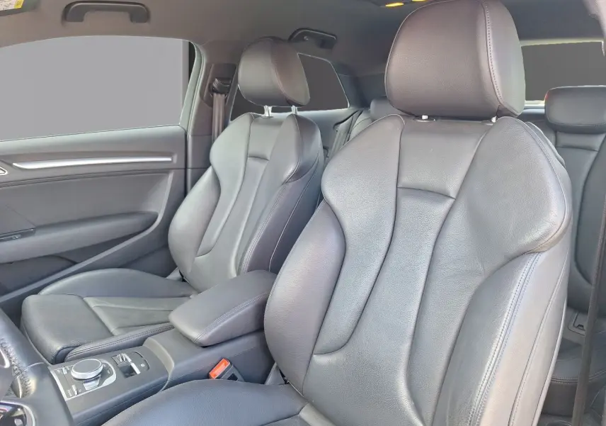 Vue intérieure des sièges avant en cuir noir de l'Audi A3 2.0 TFSI S Line, avec accoudoir central et commandes visibles.