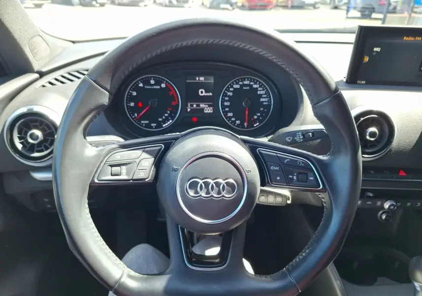 Vue intérieure centrée sur le volant cuir noir de l'Audi A3 2017 avec tableau de bord et écran multimédia visibles.