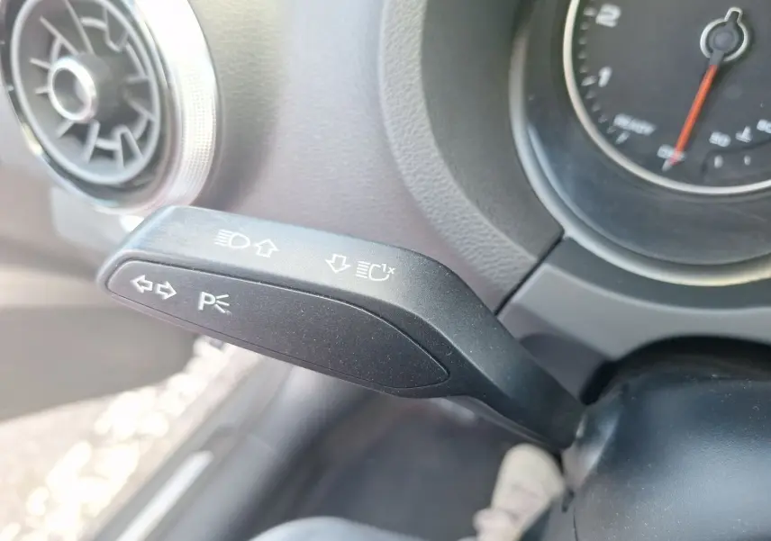 Gros plan sur la manette de clignotant noire à gauche du volant dans l’habitacle d’une Audi A3 gris 2017.