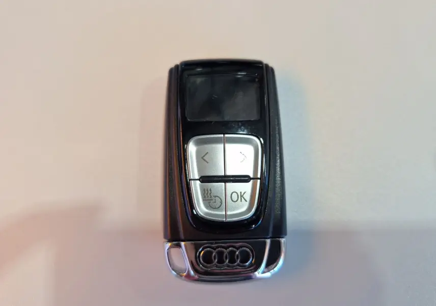 Télécommande Audi noire avec logo chromé, vue de dessus sur fond clair, boutons argentés visibles.