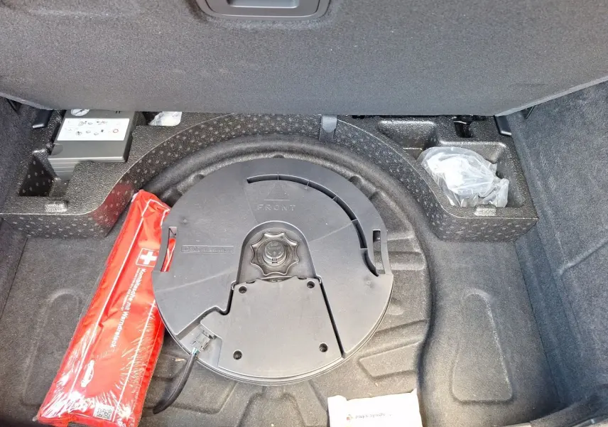 Coffre ouvert d’Audi A3 gris, vue plongeante sur la roue de secours et la trousse de secours rouge.
