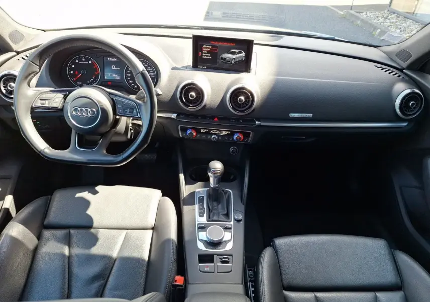 Vue intérieure avant de l'Audi A3 2017, sellerie cuir noire, tableau de bord avec écran central et volant multifonction.