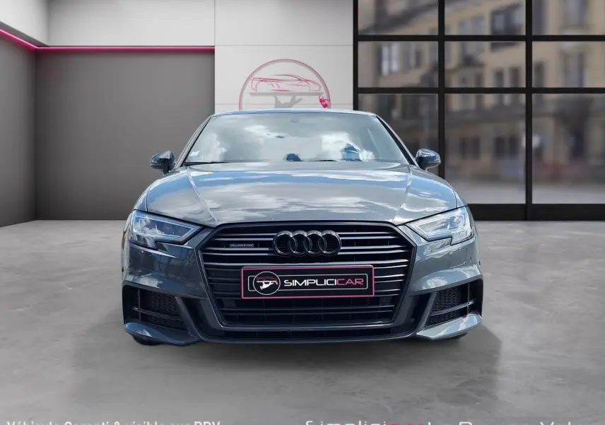 Vue frontale d'une Audi A3 gris métallisé avec calandre noire et logo Quattro visible, en intérieur showroom.