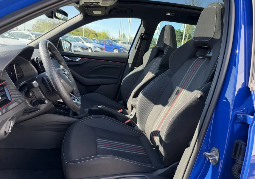Vue intérieure côté conducteur du Skoda Kamiq bleu 2025, sièges sport noirs avec surpiqûres rouges et volant cuir trois branches.