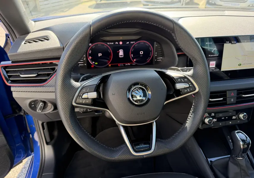 Vue intérieure centrée sur le volant sport en cuir du Skoda Kamiq bleu avec tableau de bord numérique et écran tactile.