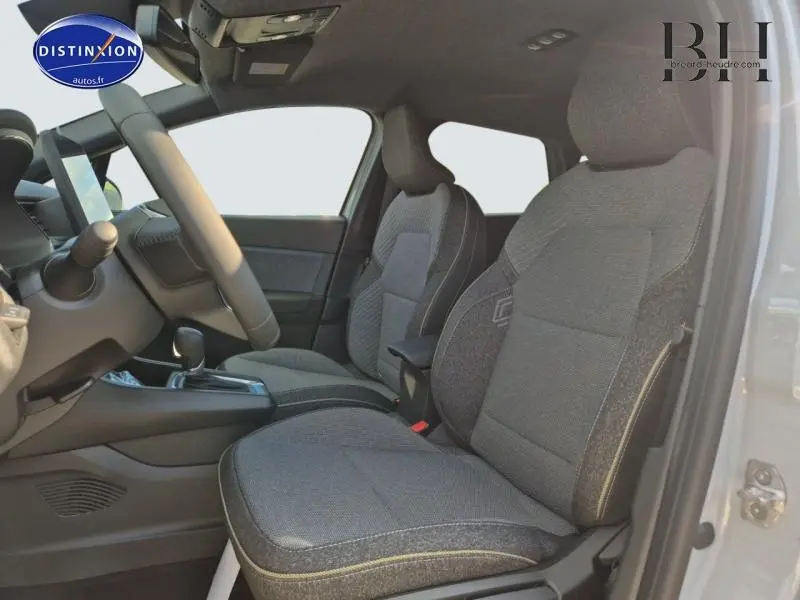 Vue intérieure côté conducteur du Renault Captur 2025, sièges tissu gris avec accoudoir central et volant multifonction.