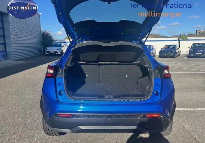 Vue arrière d'un Nissan Juke 2025 bleu magnétique métal avec coffre ouvert, montrant l'espace de chargement vide.