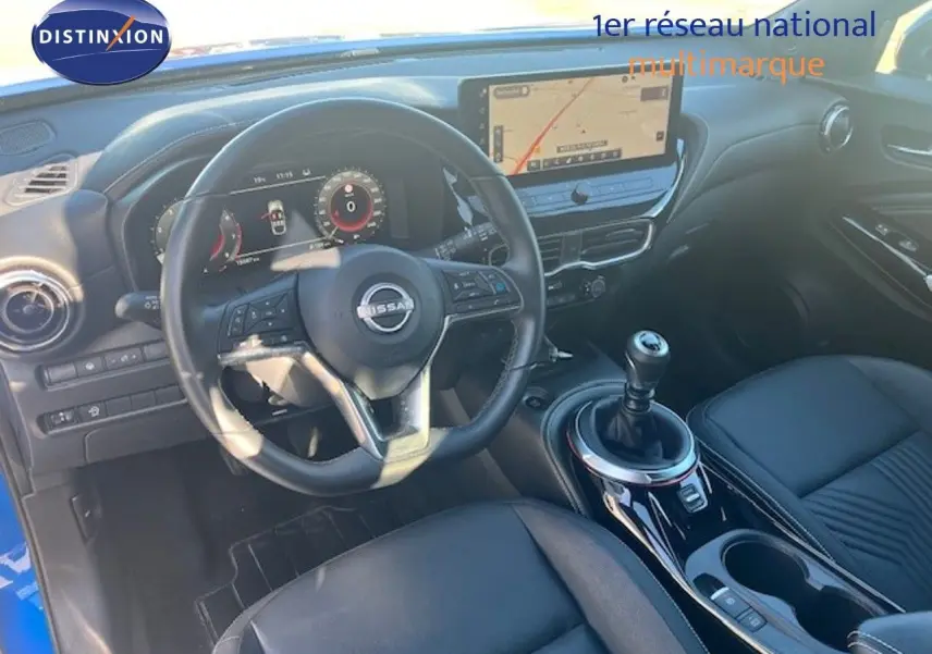 Vue intérieure du poste de conduite du Nissan Juke 2025 bleu magnétique, avec volant cuir et levier de vitesse manuel.