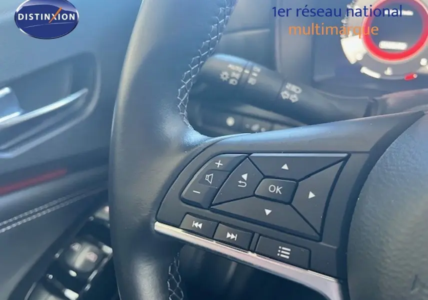Gros plan sur le volant cuir noir du Nissan Juke 2025, avec commandes multifonctions et tableau de bord partiellement visible.