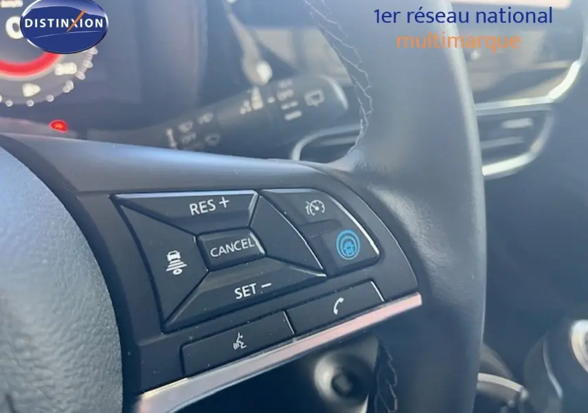 Gros plan sur les commandes au volant noir du Nissan Juke bleu magnétique, avec affichage partiel du tableau de bord.