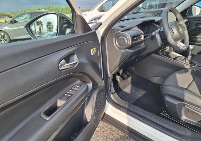 Vue intérieure côté conducteur d'un Jeep Avenger blanc 2025, montrant la porte ouverte et le tableau de bord noir.