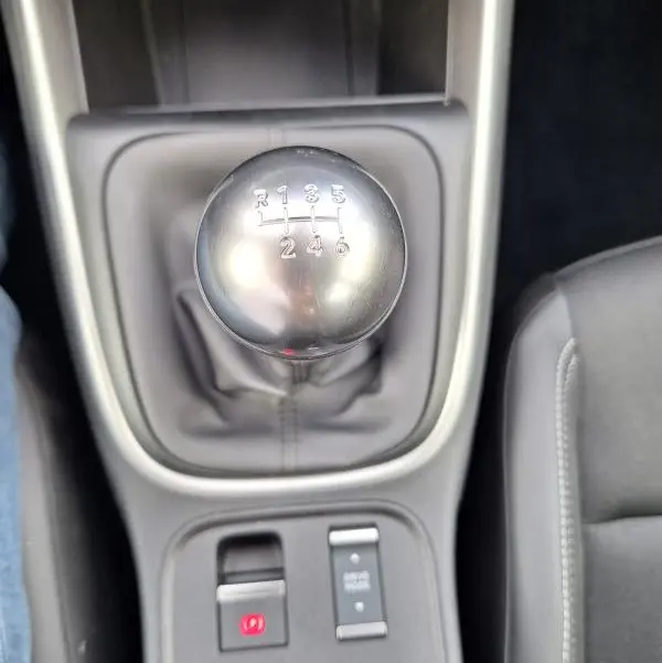 Gros plan sur le levier de vitesses manuel et la commande de frein à main électrique dans l'habitacle du Jeep Avenger blanc.