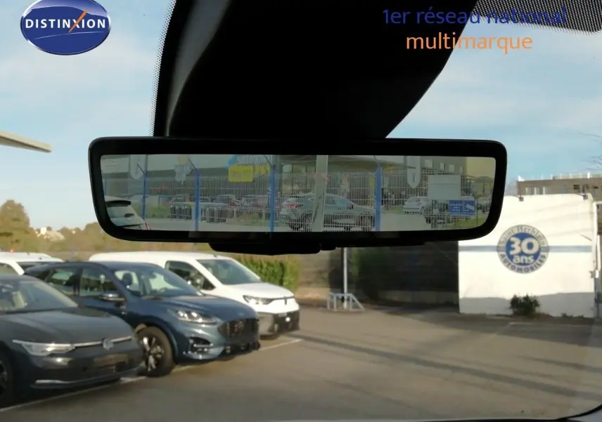 Vue depuis l'intérieur montrant le rétroviseur central d’un Citroën Berlingo blanc icy avec parking en arrière-plan.