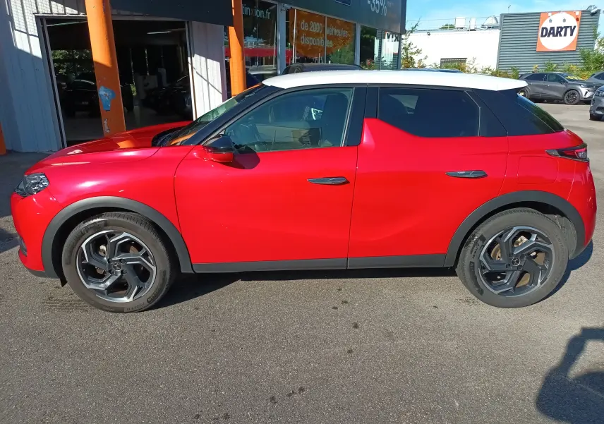 Vue de profil côté gauche d'un DS3 Crossback rouge métallisé avec toit blanc, roues 18 pouces bi-ton et poignées affleurantes.