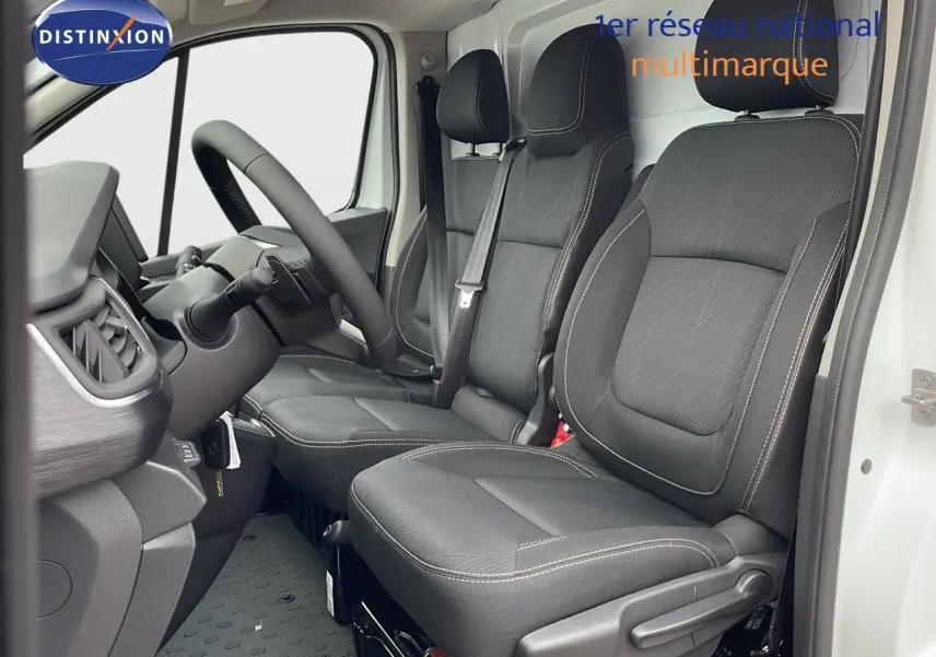 Vue intérieure côté conducteur du Renault Trafic Fourgon blanc glacier 2025, sièges noirs avec surpiqûres claires et volant visible.