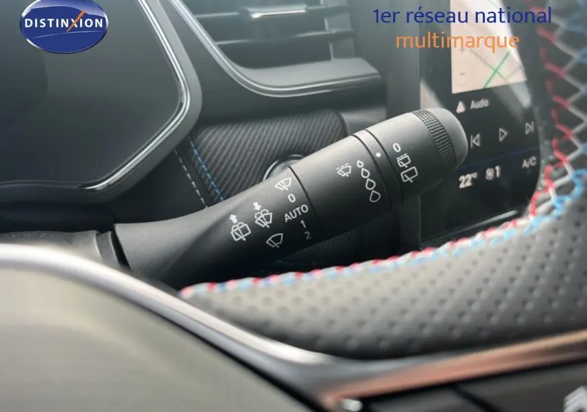 Gros plan sur la commande d’essuie-glace à gauche du volant perforé avec surpiqûres tricolores dans le Renault Symbioz blanc nacré.