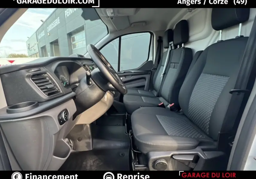 Vue intérieure côté conducteur du Ford Transit Custom blanc, montrant les sièges avant et le volant multifonction en cuir.
