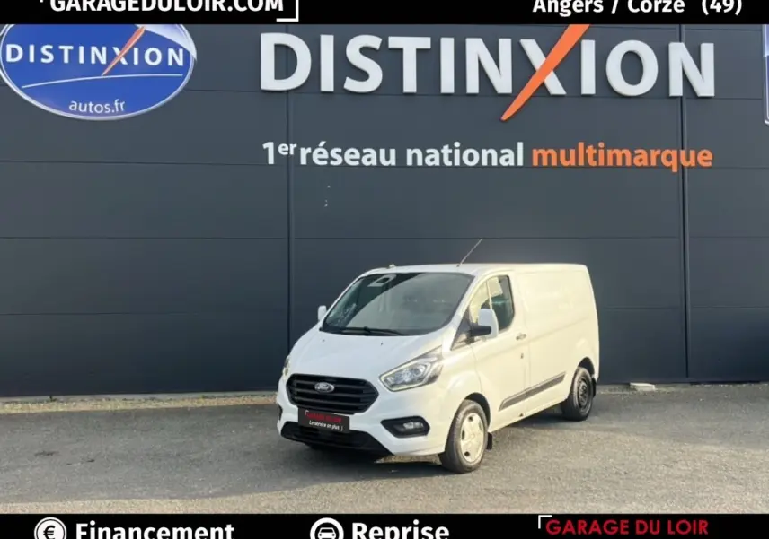 Vue 3/4 avant d'un fourgon Ford Transit Custom blanc garé devant un mur gris avec logo Distinxion.