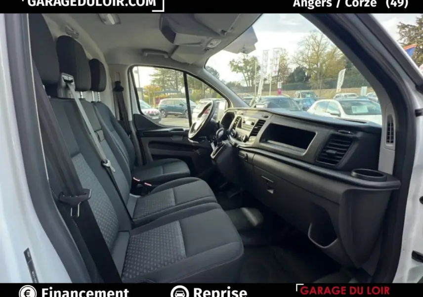Vue intérieure côté conducteur du Ford Transit Custom blanc 2023, montrant les sièges avant et le tableau de bord.