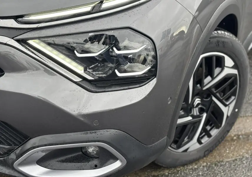 Gros plan sur l'avant droit gris Platinium du Citroën C4 2024, mettant en valeur le phare LED et la jante alliage 18 pouces.