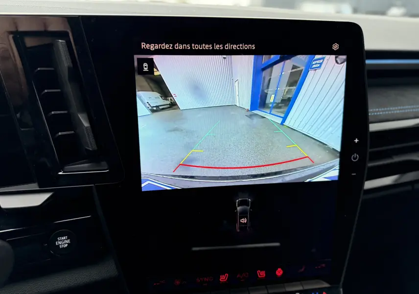 Écran central du Renault Austral 2025 montrant la caméra de recul avec vue arrière sur un sol gris et un bâtiment bleu.