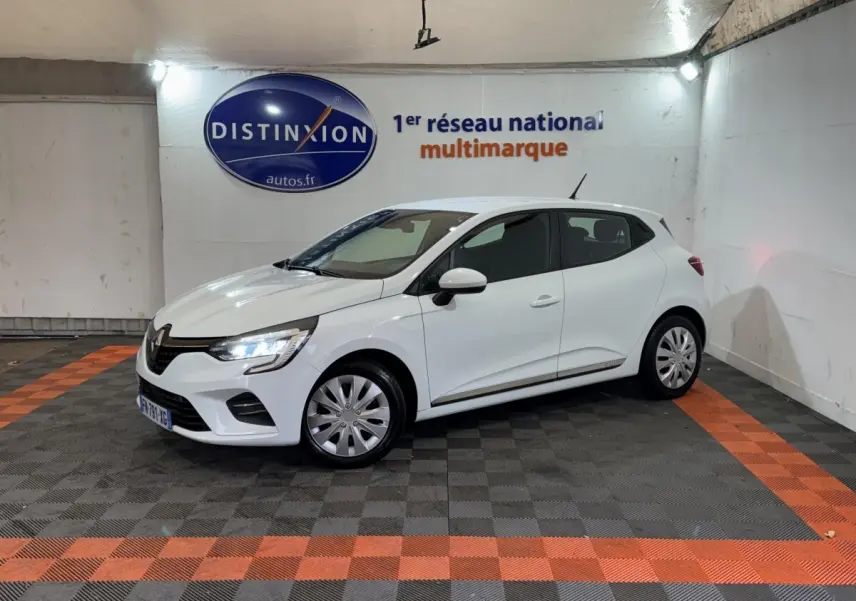 Renault Clio Business TCe 100 blanc vue 3/4 avant droit, phares LED allumés, stationnée en intérieur sur sol damier noir et orange.