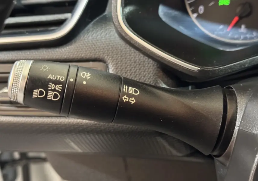 Gros plan sur la manette de commande des phares et clignotants dans l'habitacle d'une Renault Clio Business blanche de 2020.