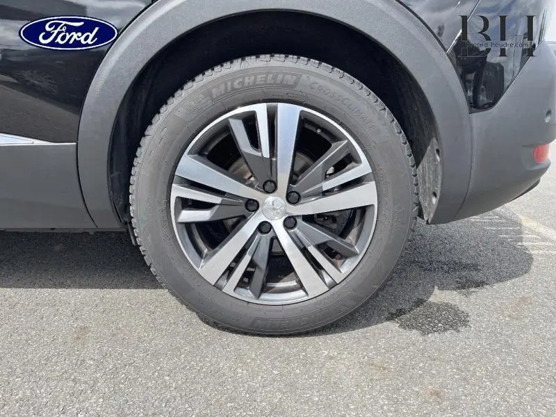 Gros plan sur la roue avant droite noire Perla Nera du Peugeot 5008 avec jante alu et logo Peugeot central.