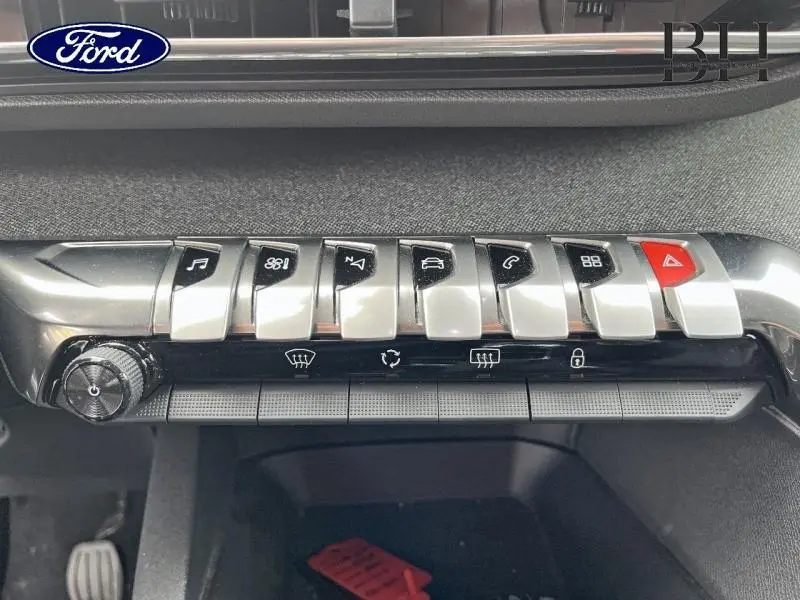 Gros plan sur la rangée de boutons chromés et noirs de la console centrale du Peugeot 5008 noir Perla Nera, avec bouton d'alerte rouge.