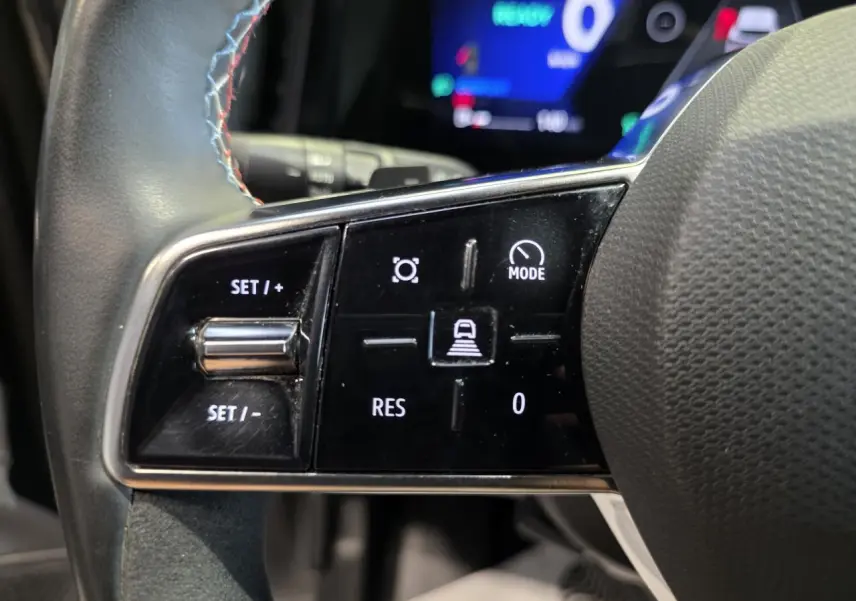 Gros plan sur les commandes du volant à gauche du Renault Austral gris foncé, avec insert Alcantara et surpiqûres bleues.