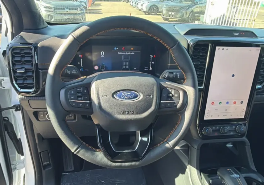 Vue intérieure centrée sur le volant cuir multifonctions avec coutures orange du Ford Ranger blanc, écran tactile vertical visible.