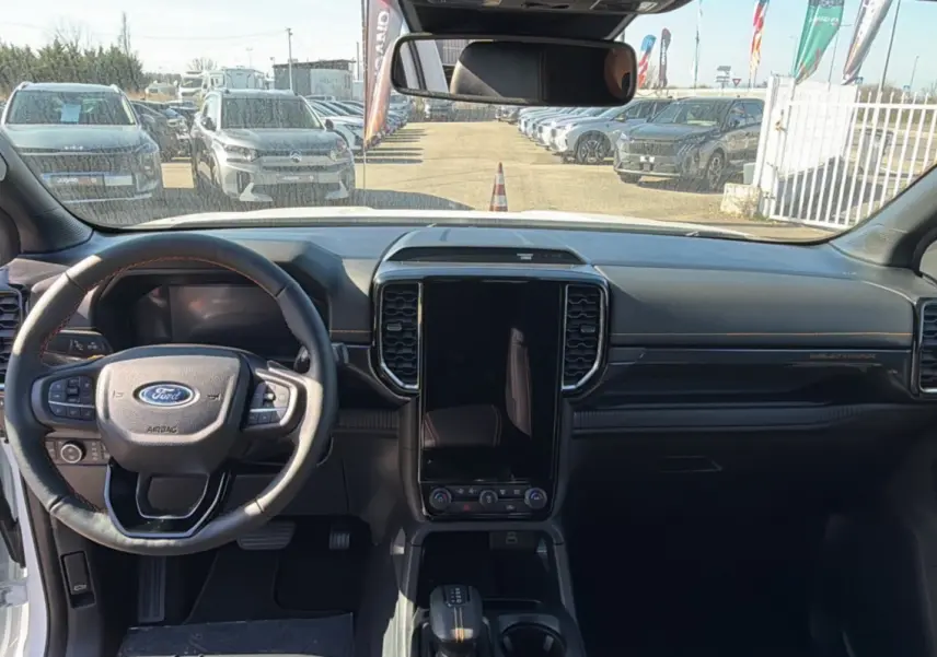 Vue intérieure frontale du Ford Ranger Wildtrak 2025, avec tableau de bord noir et grand écran tactile vertical central.