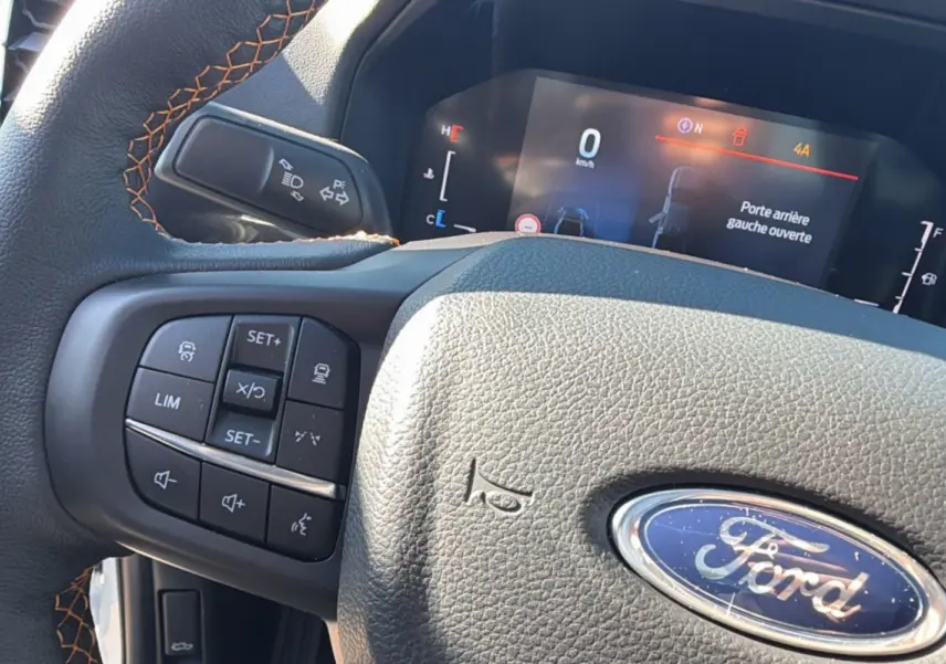 Gros plan sur le volant cuir noir avec surpiqûres orange et tableau de bord digital du Ford Ranger blanc 2025.