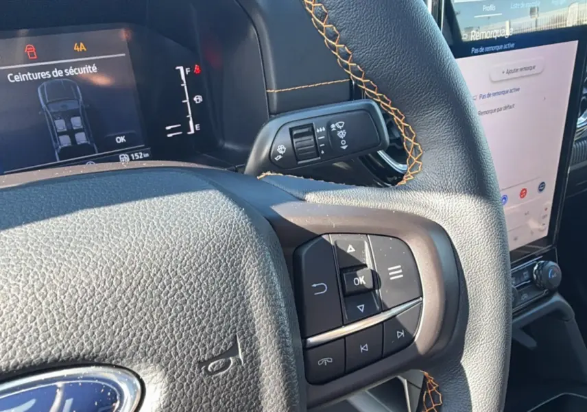 Gros plan sur le volant cuir noir avec surpiqûres orange du Ford Ranger 2025, affichage numérique et écran tactile visible.