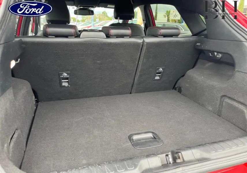 Vue du coffre ouvert du Ford Puma rouge Premium Lucid, montrant la banquette arrière rabattable et l'espace de chargement.