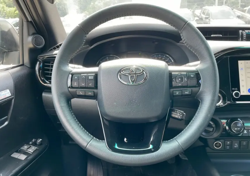 Vue intérieure centrée sur le volant noir du Toyota Hilux 4x4 Invincible 2025 avec commandes intégrées et tableau de bord visible.