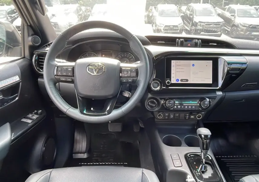 Vue intérieure frontale du tableau de bord du Toyota Hilux 4x4 blanc 2025 avec volant multifonction et écran tactile central.