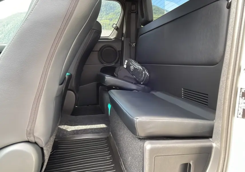 Vue intérieure arrière côté droit du Toyota Hilux 4x4 blanc 2025, siège rabattable en cuir noir et rangement avec trousse Toyota.