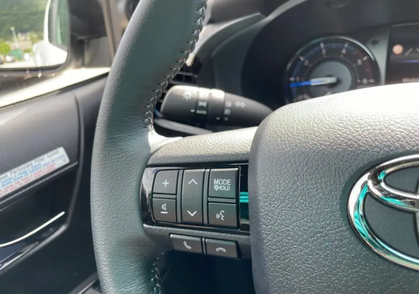 Gros plan sur le volant du Toyota Hilux 2025 blanc, montrant les commandes multifonctions côté gauche et le logo Toyota.