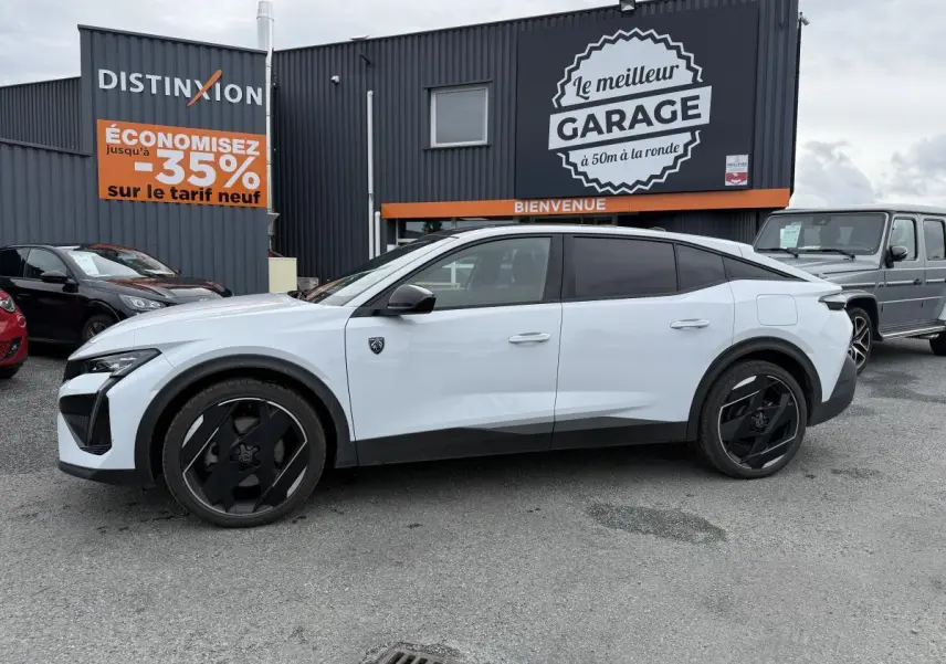 Vue de profil côté gauche d'une Peugeot 408 blanche avec jantes noires et détails noirs brillants sur un parking devant un garage.