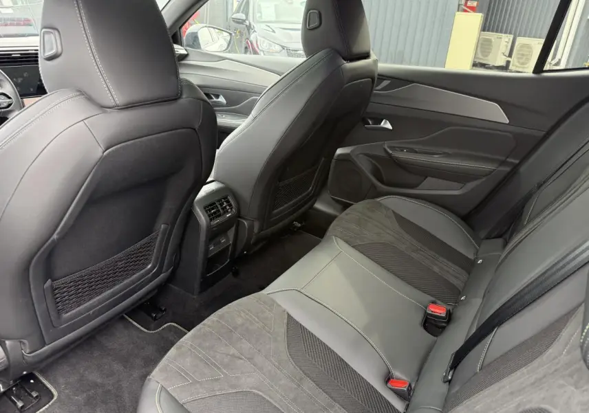Vue arrière intérieure de la Peugeot 408 2024, sièges arrière en tri-matière gris avec surpiqûres vertes et aérations centrales.