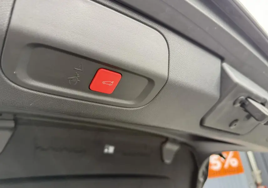 Bouton rouge d'ouverture motorisée du hayon sur le bord intérieur du coffre d'une Peugeot 408 blanche 2024.