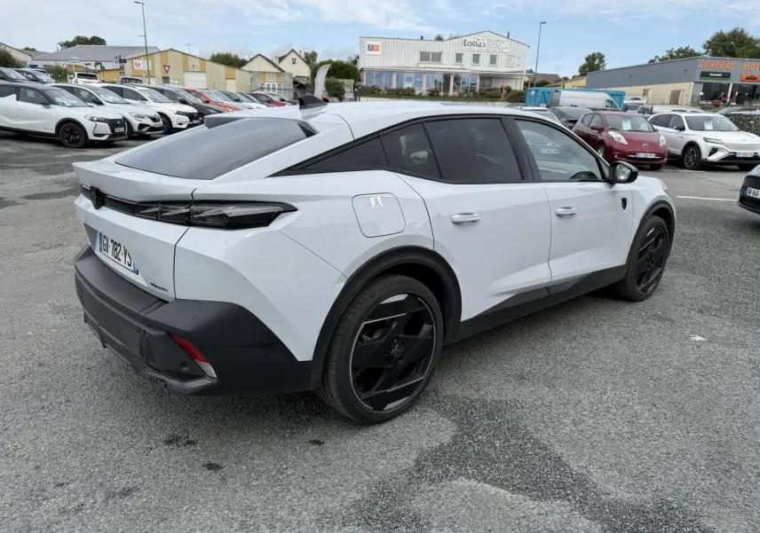 Vue 3/4 arrière droite d'une Peugeot 408 blanche avec jantes noires et toit noir Mistral sur parking extérieur.