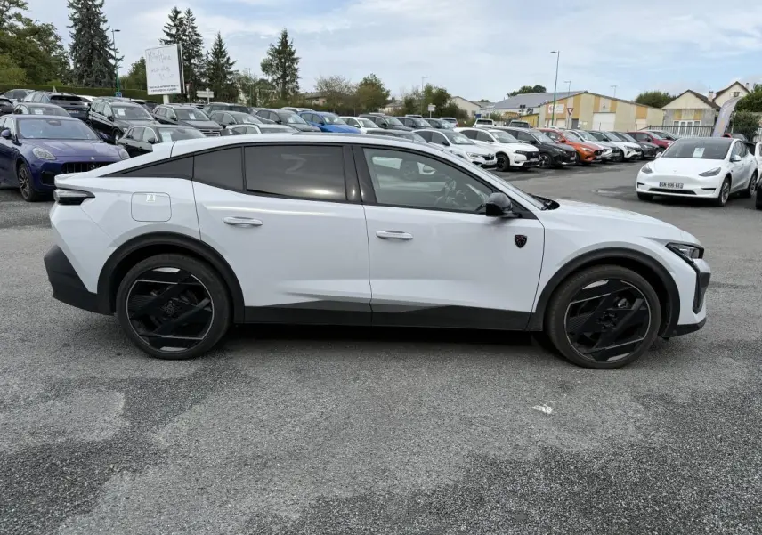 Profil côté gauche d'une Peugeot 408 blanche 2024 avec jantes noires et vitres teintées sur parking.