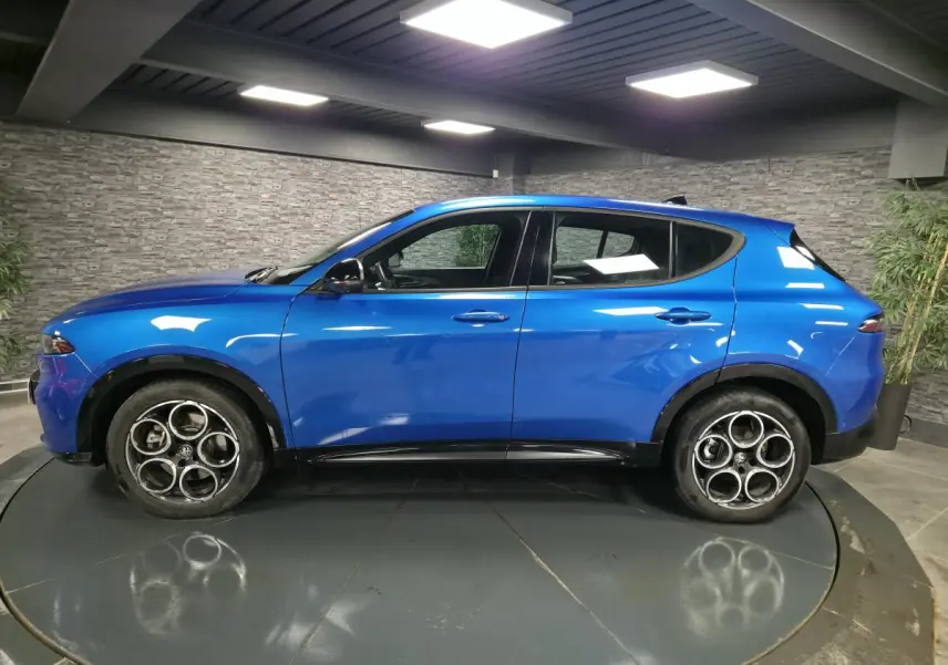 Vue de profil côté gauche d'un Alfa Romeo Tonale bleu métallisé avec jantes alliage 18 pouces dans un showroom.