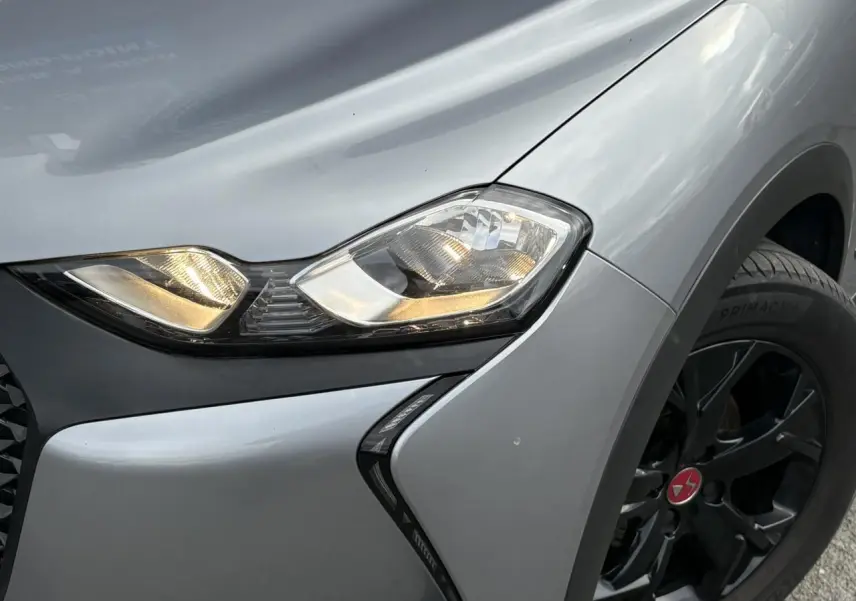 Gros plan sur le phare avant droit et la roue noire du DS3 Crossback gris Artense, mettant en valeur le design anguleux.