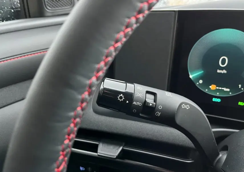 Vue rapprochée du commodo d’éclairage à gauche du volant noir avec surpiqûres rouges dans l’habitacle du Hyundai Tucson 2025.