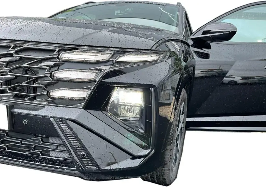Vue avant droite rapprochée du Hyundai Tucson 2025 noir brillant avec porte ouverte et phares allumés sous la pluie.