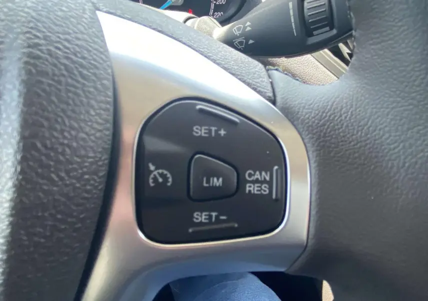 Gros plan sur les commandes du régulateur de vitesse au volant cuir noir du Ford Tourneo Courier blanc, version 2022.